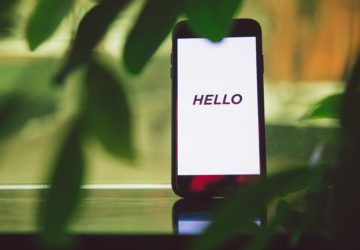 Smartphone avec une mention "Hello" sur un écran blanc et derrière plusieurs plantes vertes.